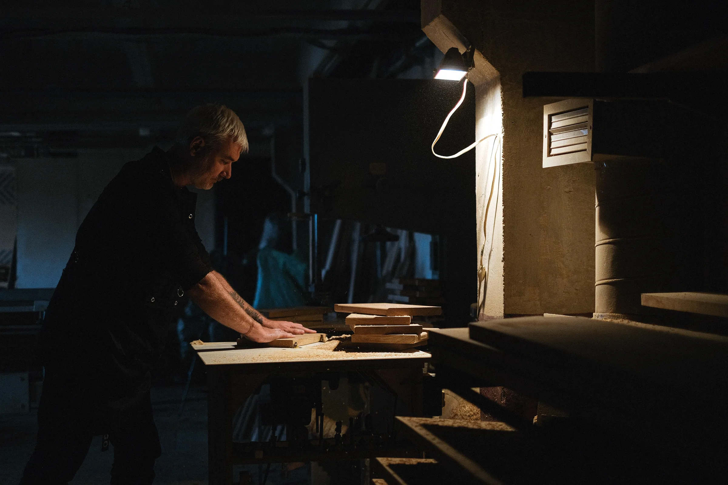 A craftsman working intently at a lit bench in a workshop after dark.