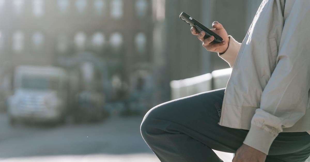 Someone using a phone outdoors in bright daylight beside a city road.