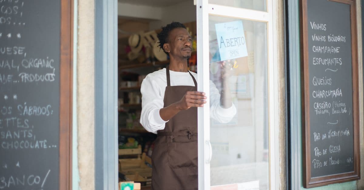 A shop owner in an apron opening up his business for the day's trade.