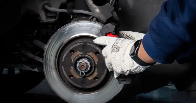 Mechanic working on car brake system in a workshop setting.