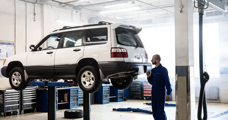 Mechanic inspecting a lifted SUV in a modern auto repair garage.