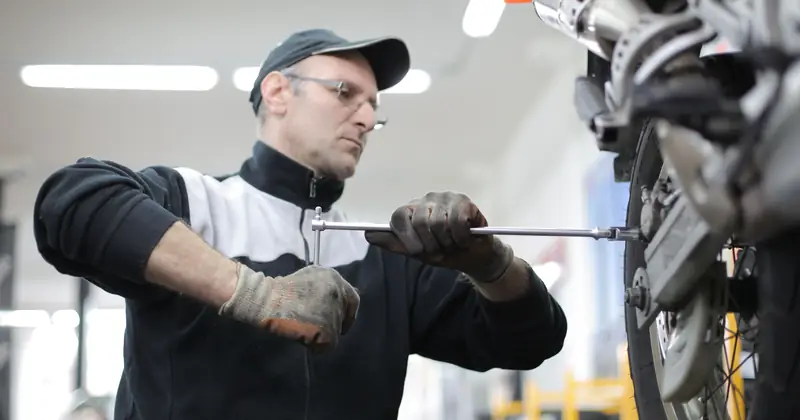 Man skillfully fixes a motorcycle tire using a wrench in an indoor workshop setting.
