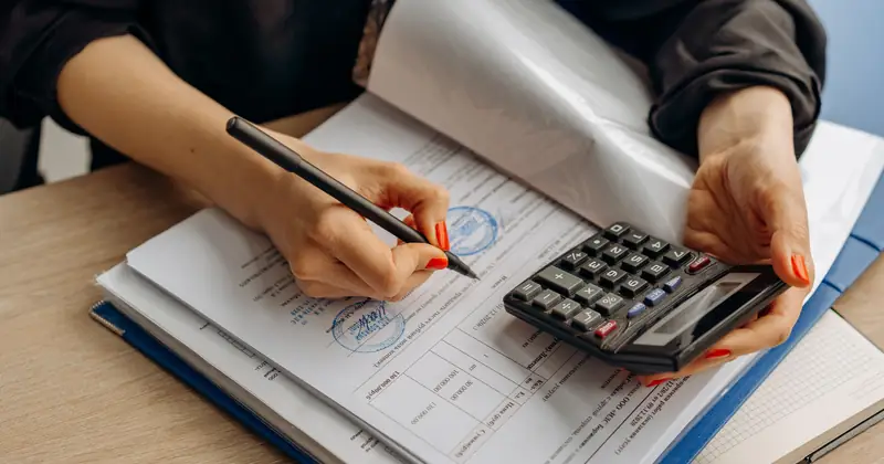 An accountant using a calculator and signing paperwork, showcasing financial analysis.