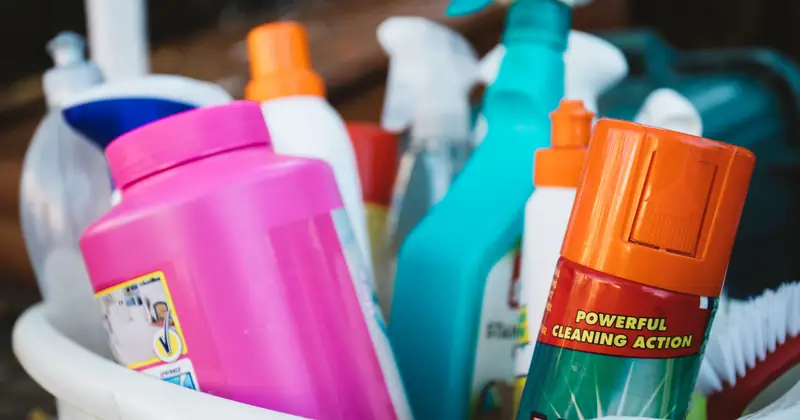 Close-up of assorted cleaning supplies in a bucket outdoors, showcasing various detergents and sprays.