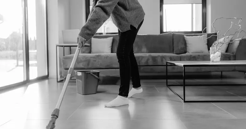 A grayscale photo of a person mopping the floor in a modern living room.