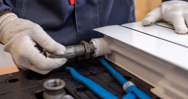 Close-up of a plumber installing a radiator pipe using specialized tools.