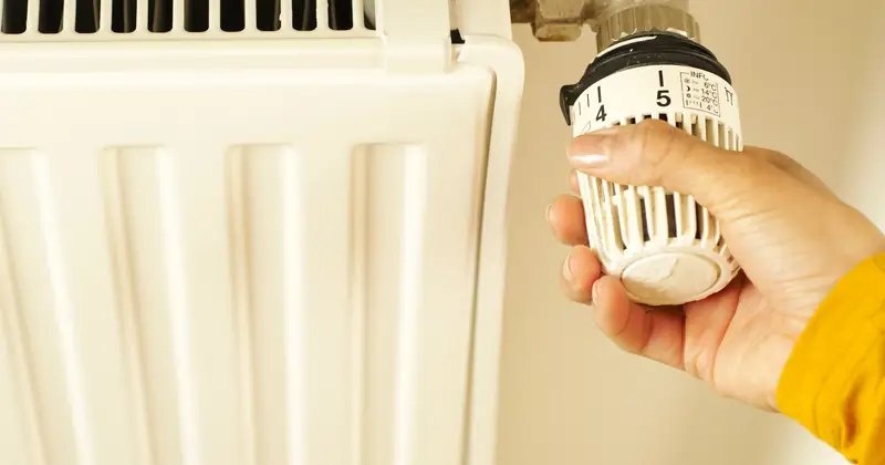 Close-up of hand adjusting radiator thermostat to control home heating temperature.