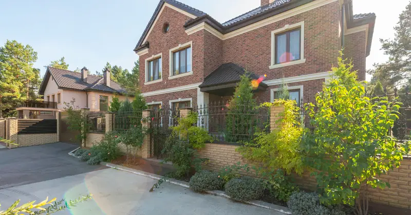 Elegant brick house with a lush garden and driveway, under a clear sky.