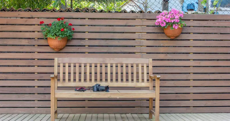 A wooden bench with potted flowers against a wooden fence in a peaceful backyard setting.