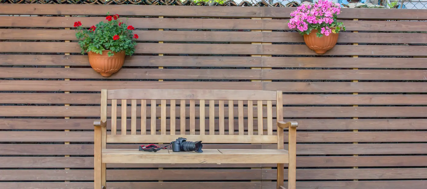A wooden bench with potted flowers against a wooden fence in a peaceful backyard setting.