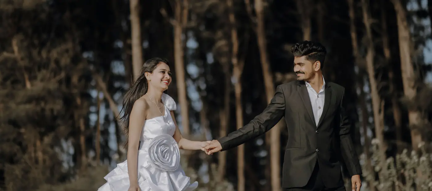 From above side view of groom holding happy bride with flower bouquet by hand while looking at each other on stone surface near rippled ocean on wedding day