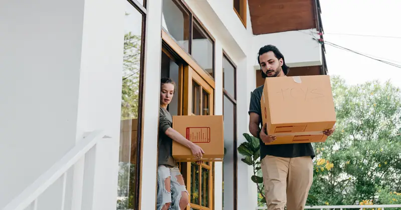 Young diverse male and female in modern casual outfits with cardboard boxes in hands watching step while moving out of old house on summer day