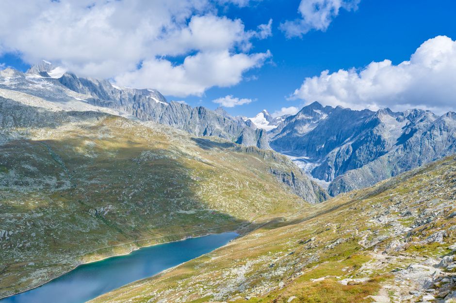 A clear mountain lake below snow-topped Alpine peaks.