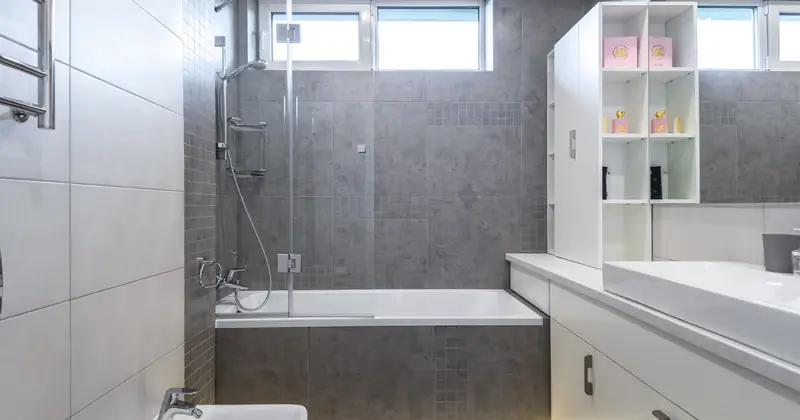 Contemporary bathroom featuring sleek gray tiles, bathtub, shower, and vanity.