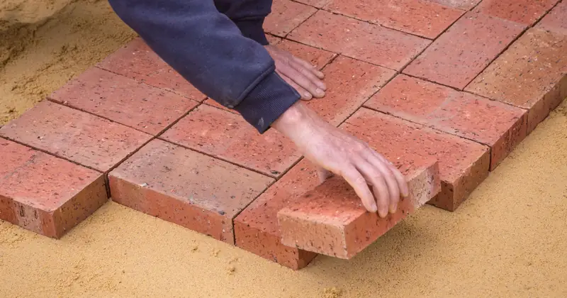 From above crop unrecognizable construction worker in uniform laying bricks on ground in daylight