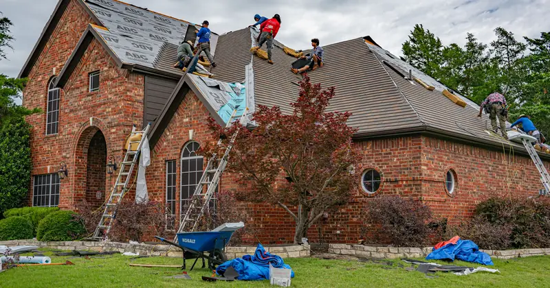 Roofers working on brick home in Allen, Texas, addressing shingles and roofing materials.