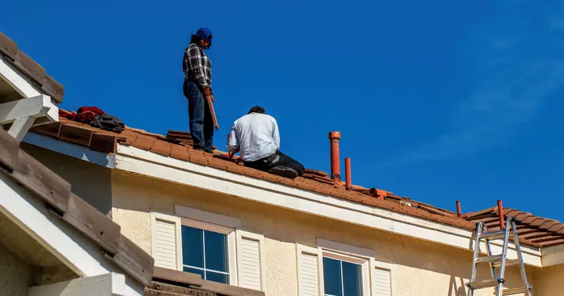 Roof construction scene with workers on a tiled roof, captured under a clear blue sky.