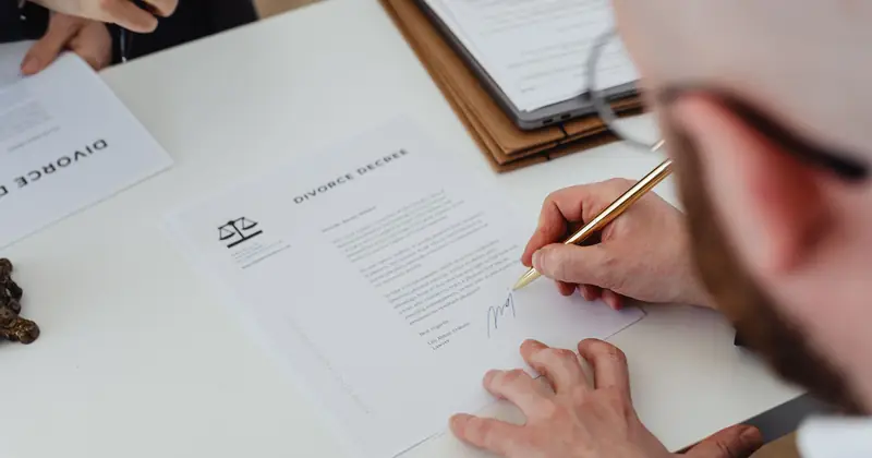 Close-up of a person signing a divorce decree on a desk.