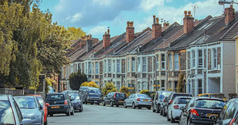 Picturesque view of parked cars along classic English townhouses under a blue sky.