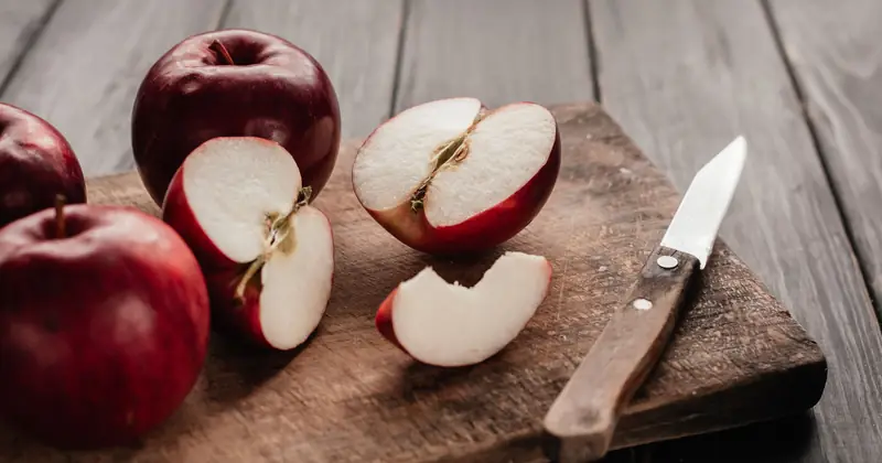 Top view of fresh red apples sliced on a rustic wooden chopping board with a knife.