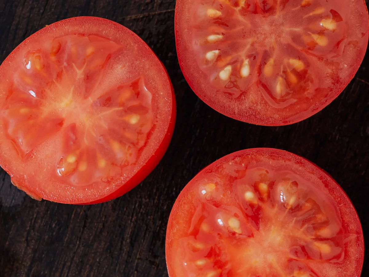 Fresh tomato halves showing their juicy red flesh and pale seed chambers on a dark wooden board.