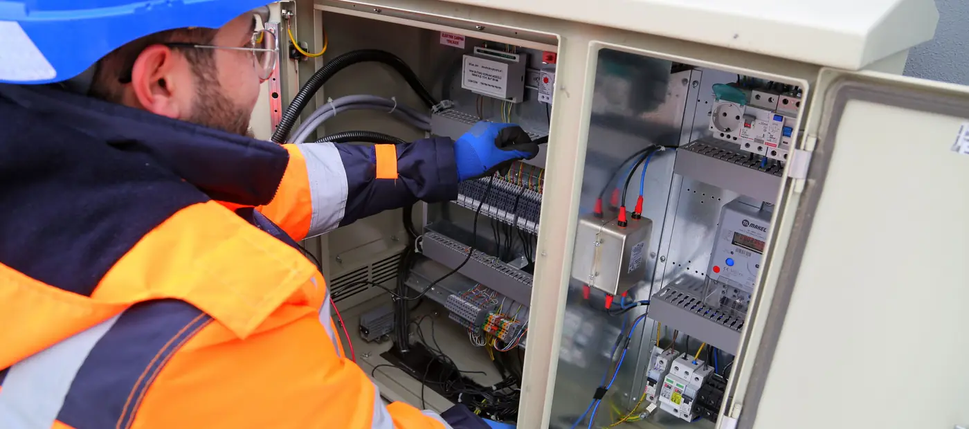 Engineer in safety gear working on an outdoor electrical panel, ensuring system functionality.