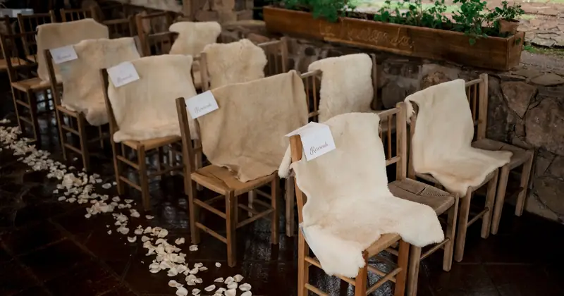 Cozy wedding seating arrangement outdoors with wooden chairs and soft fur covers.
