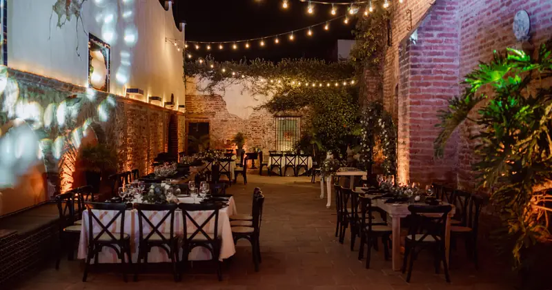 Charming outdoor event setting at night, featuring tables with elegant decor under warm string lights.