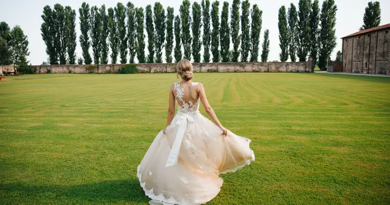 A bride in a stunning gown gracefully walks across a lush garden in Italy, capturing elegance and romance.