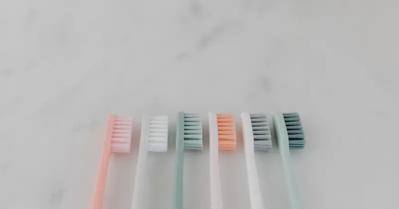 A row of colorful pastel toothbrushes aligned on a smooth marble surface.
